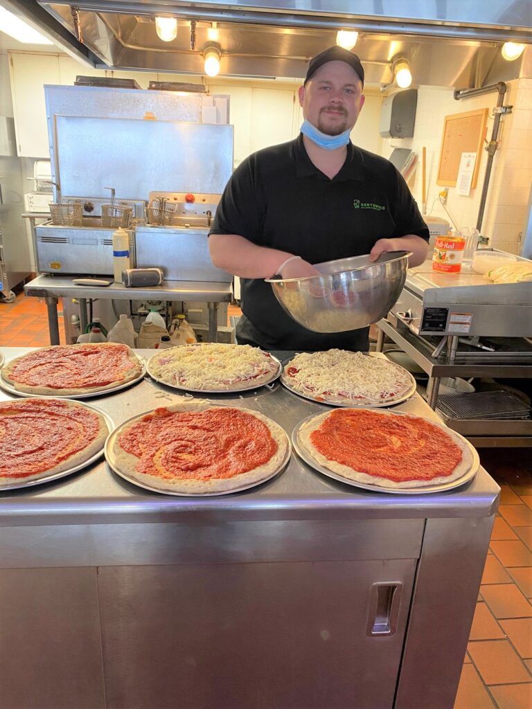 Man putting cheese onto uncooked pizzas