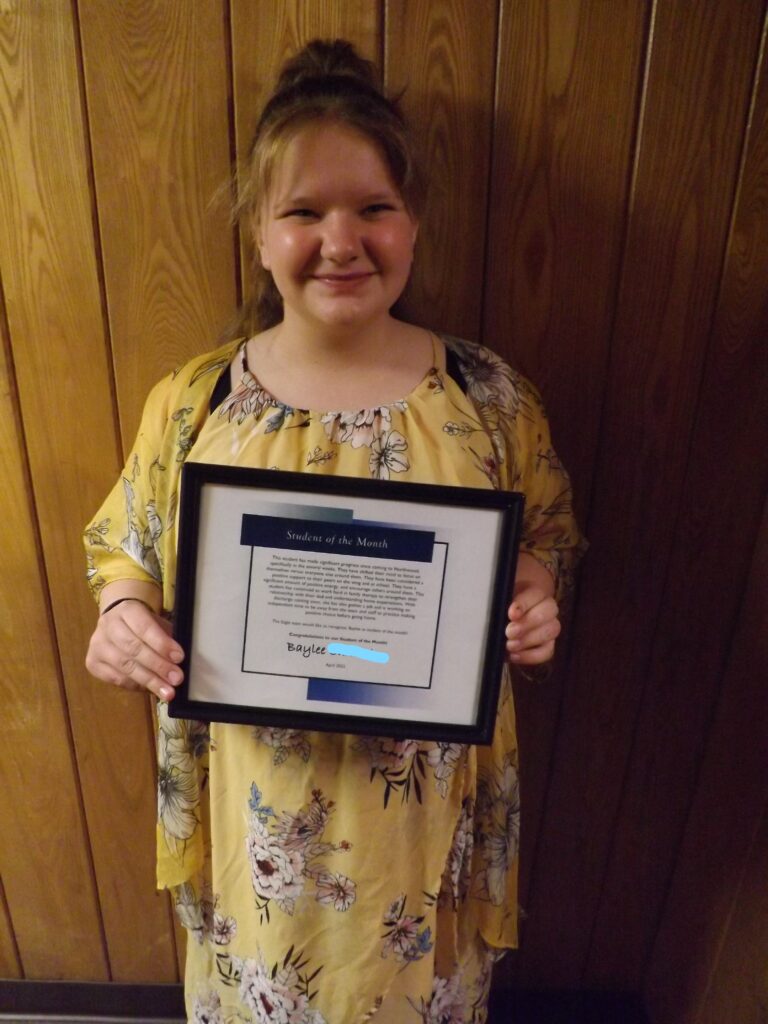 Person holding up "student of the month" award with wood paneling in the background